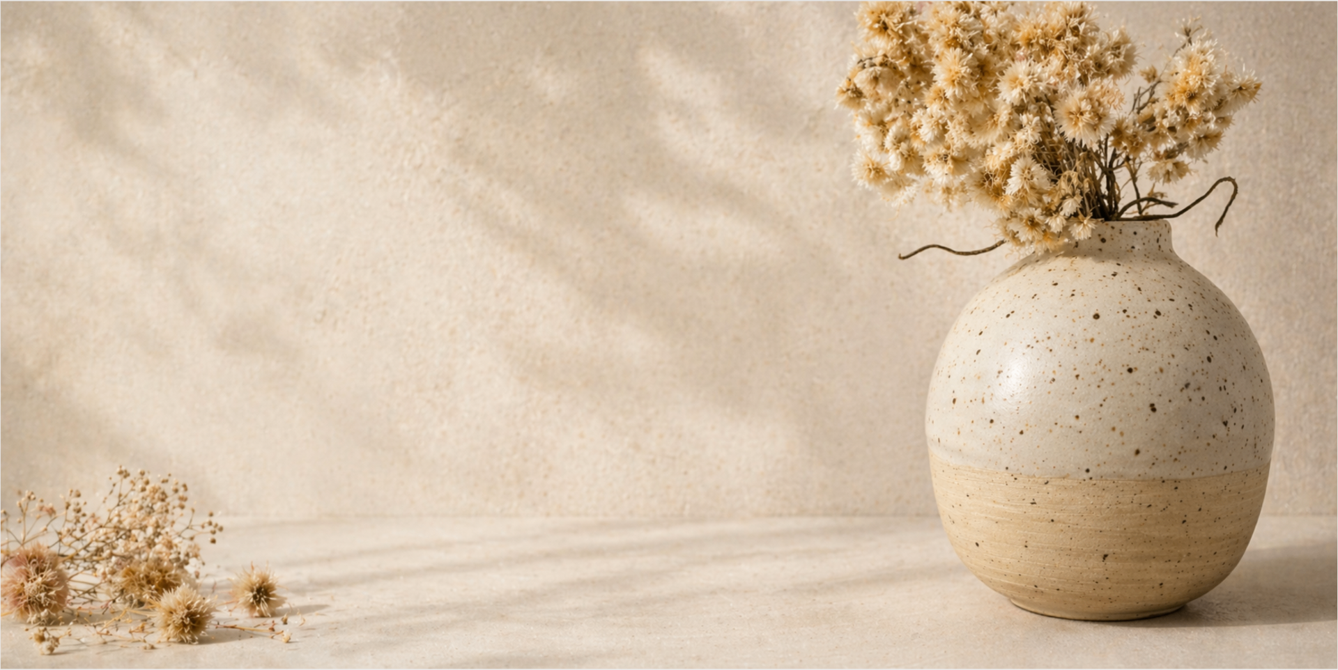 Speckled stoneware vase with dried flowers on a warm cream backdrop